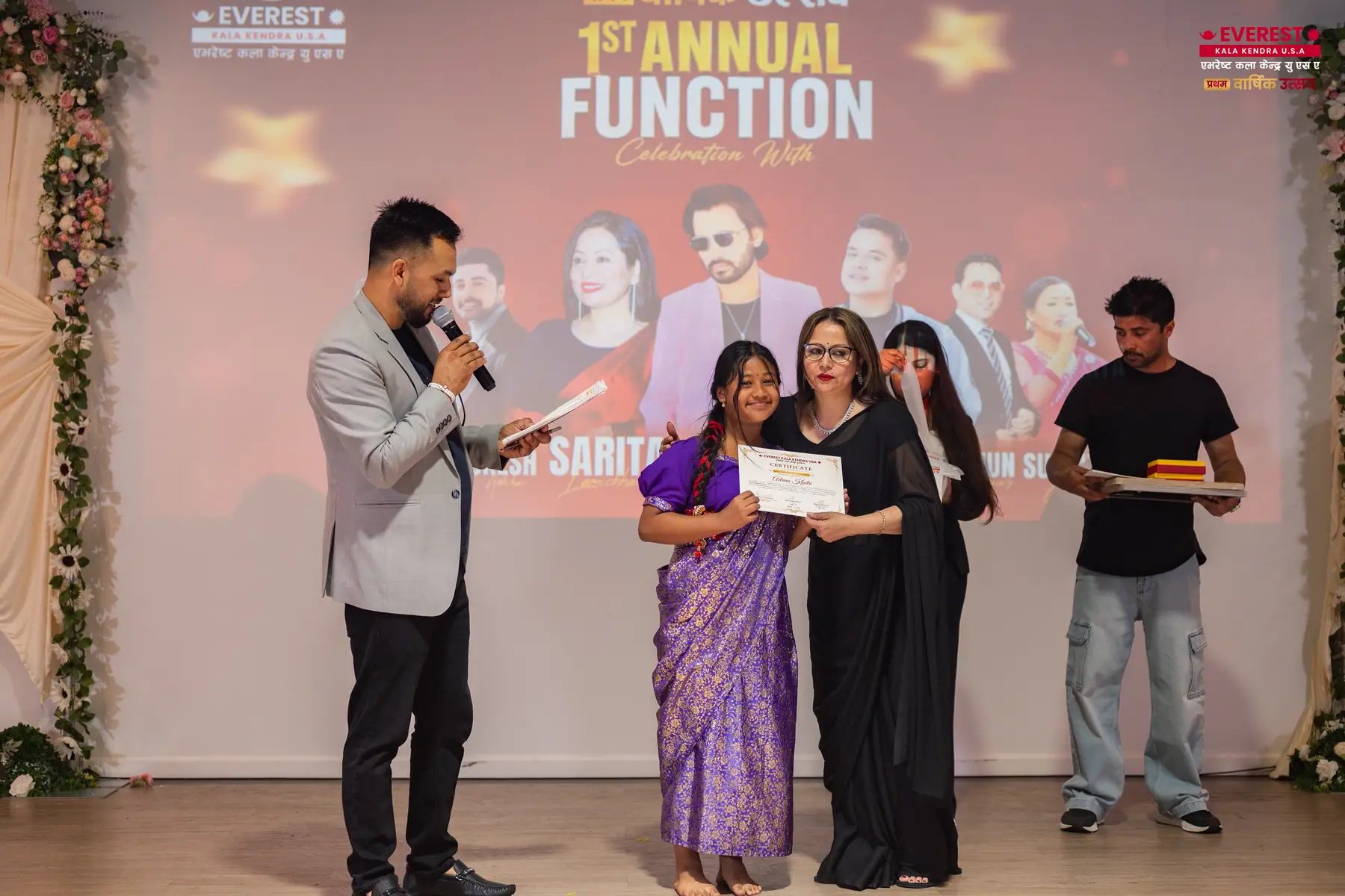 EKK students receiving certificates on stage while the host speaks into a microphone
