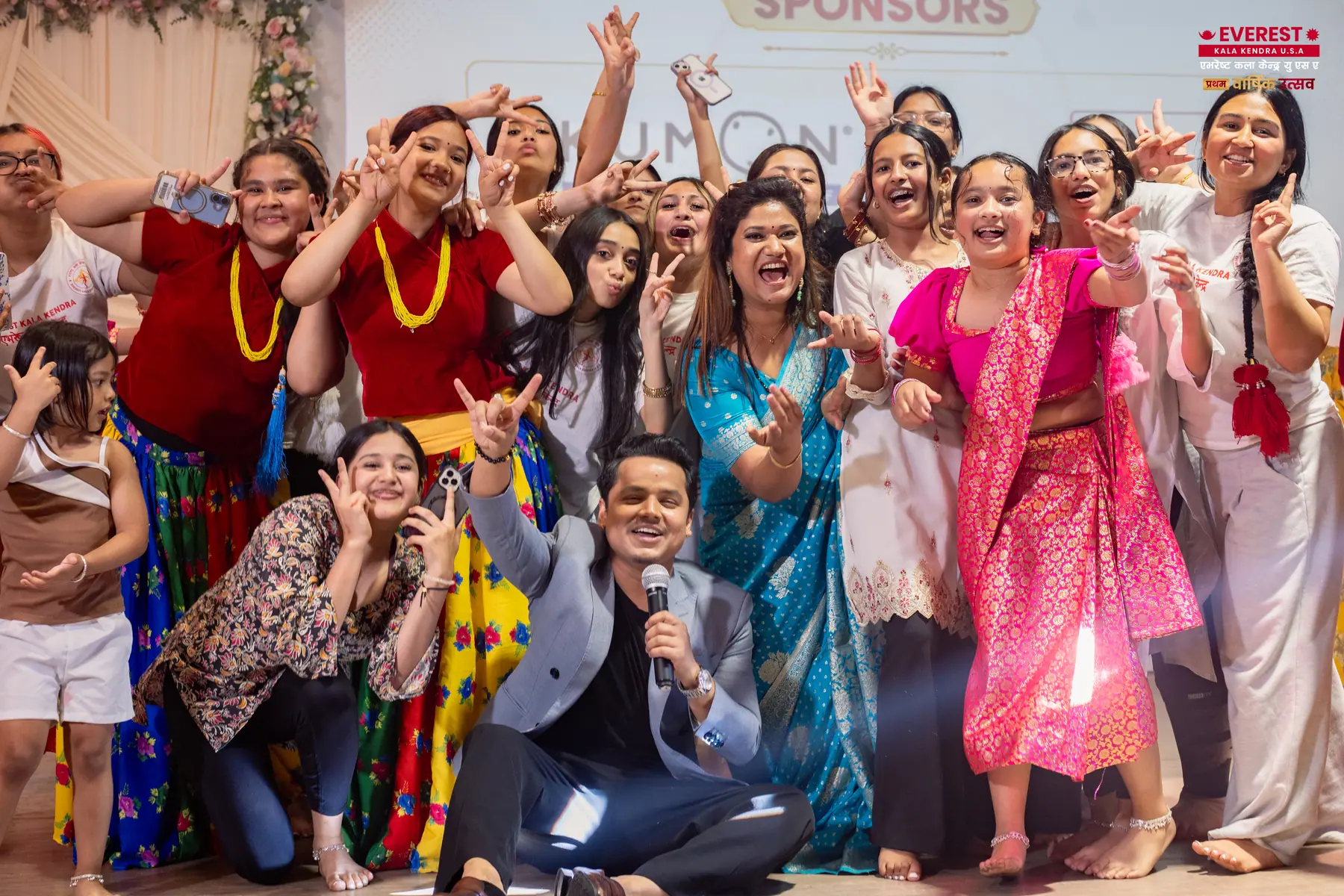 A large group of EKK performers in colorful traditional dress celebrating together on stage