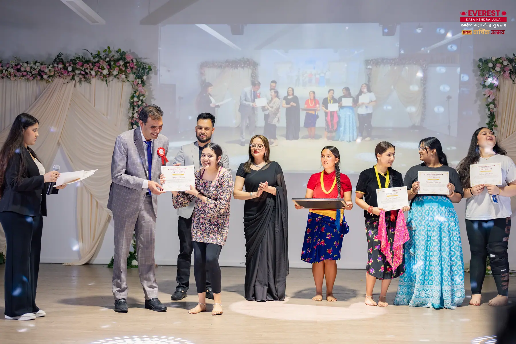 EKK students standing in a line on stage holding achievement certificates