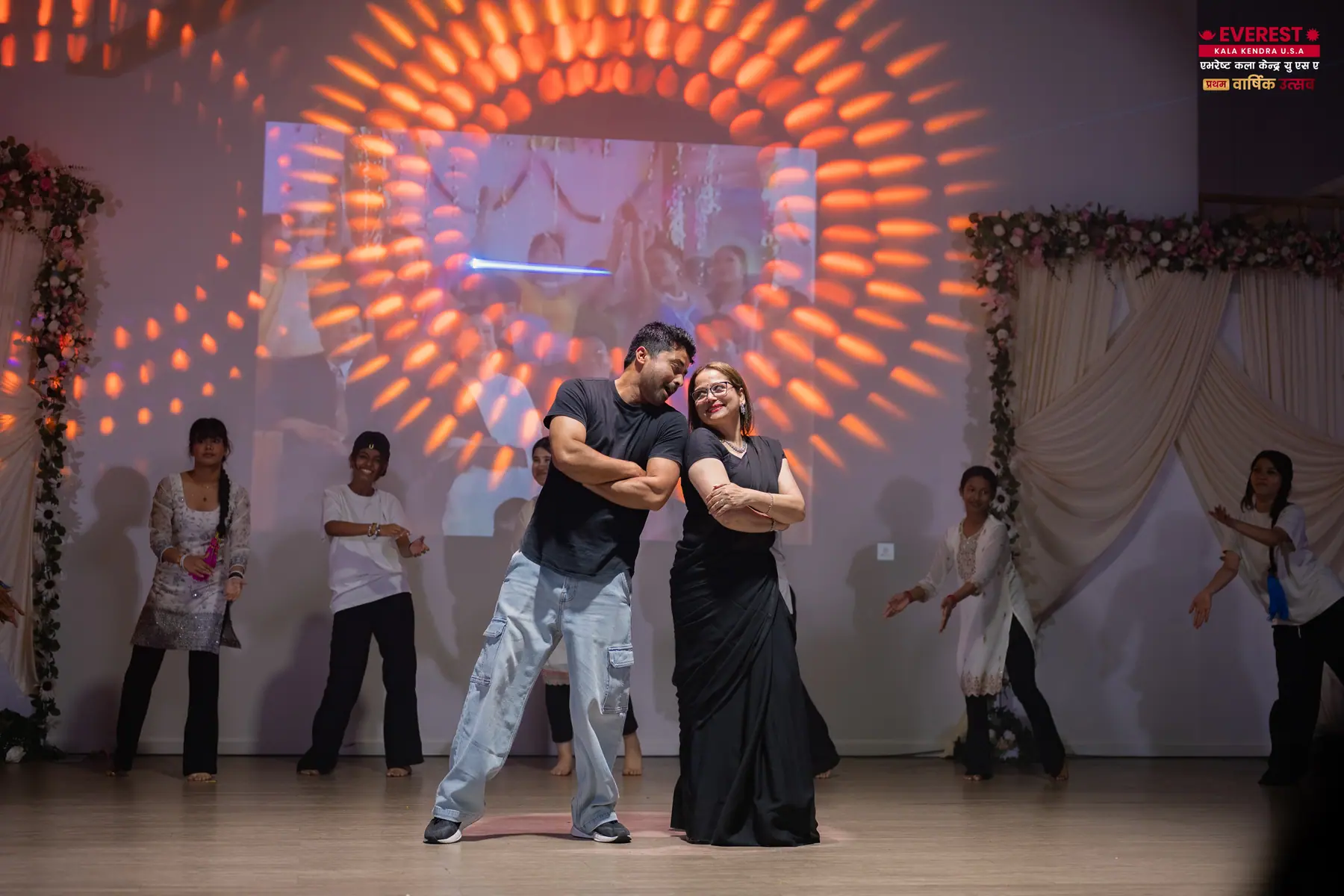 Two EKK performers dancing as a pair in front of a decorated stage backdrop