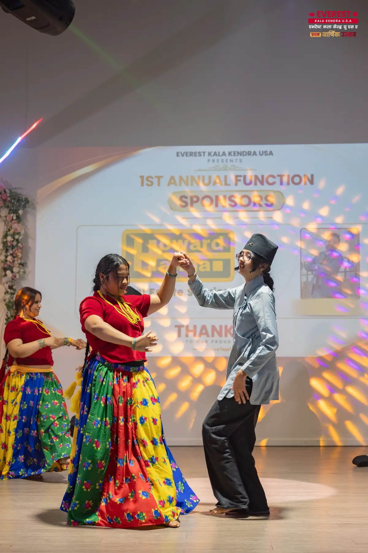 Two EKK dancers performing together in front of the annual function sponsor screen