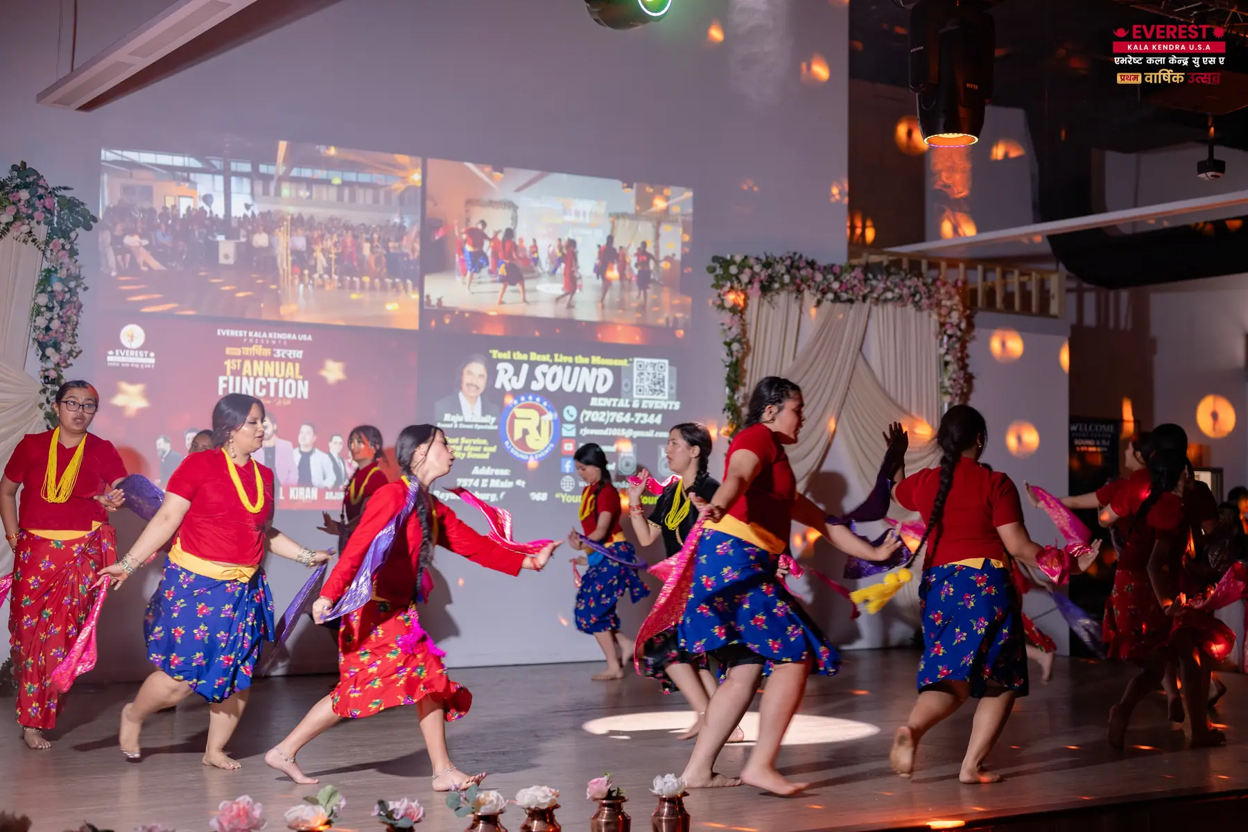 A line of EKK students in colorful traditional Nepali dress performing a group dance on stage