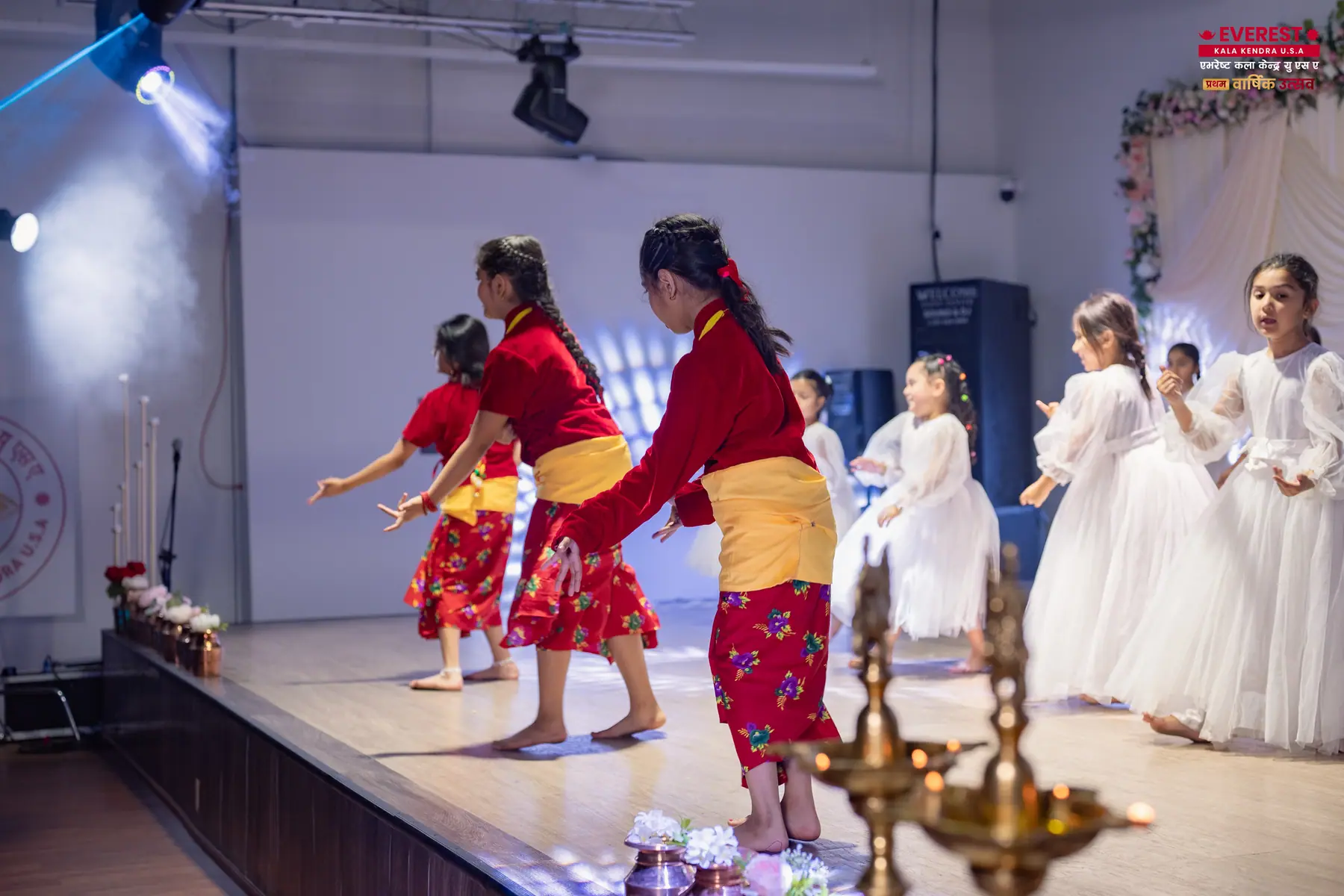 EKK performers in red and white traditional dress dancing around lit oil lamps on stage