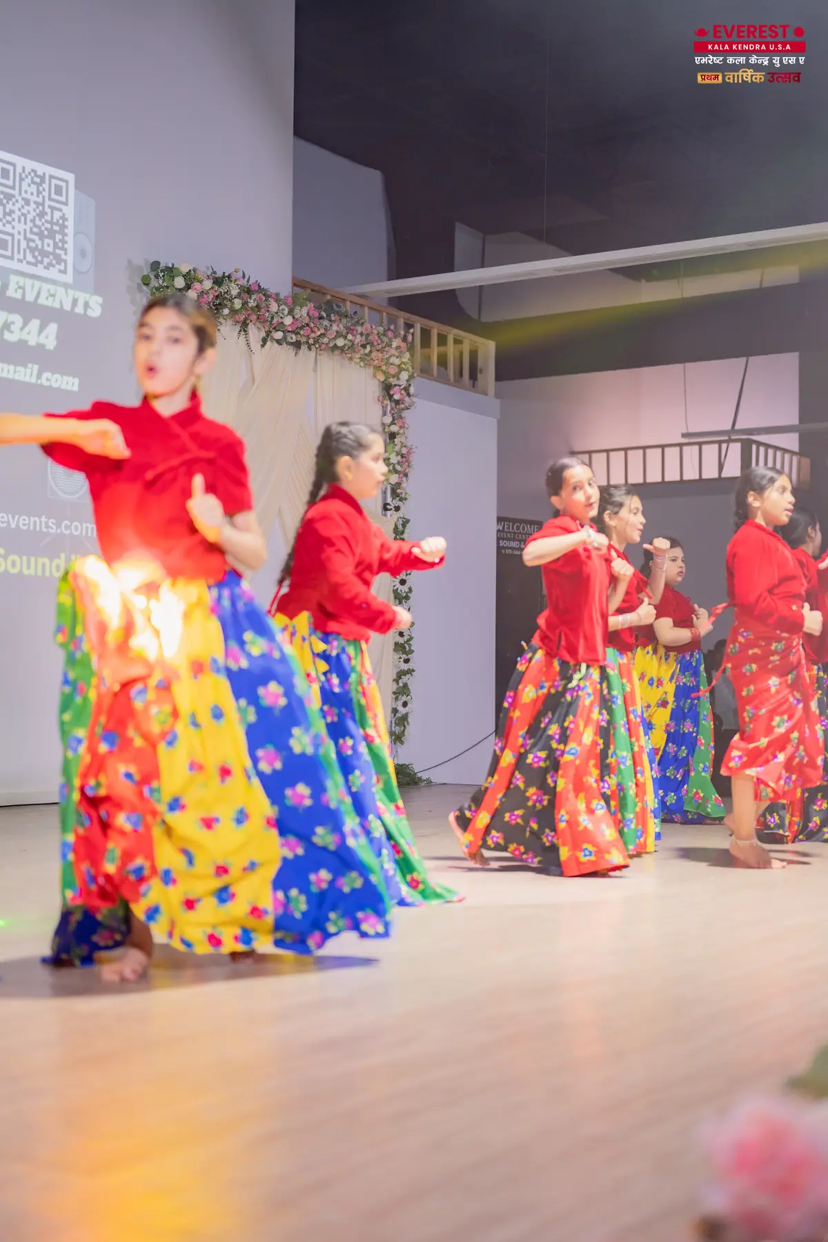 An EKK dancer in a red blouse and colorful skirt performing a solo under stage lighting