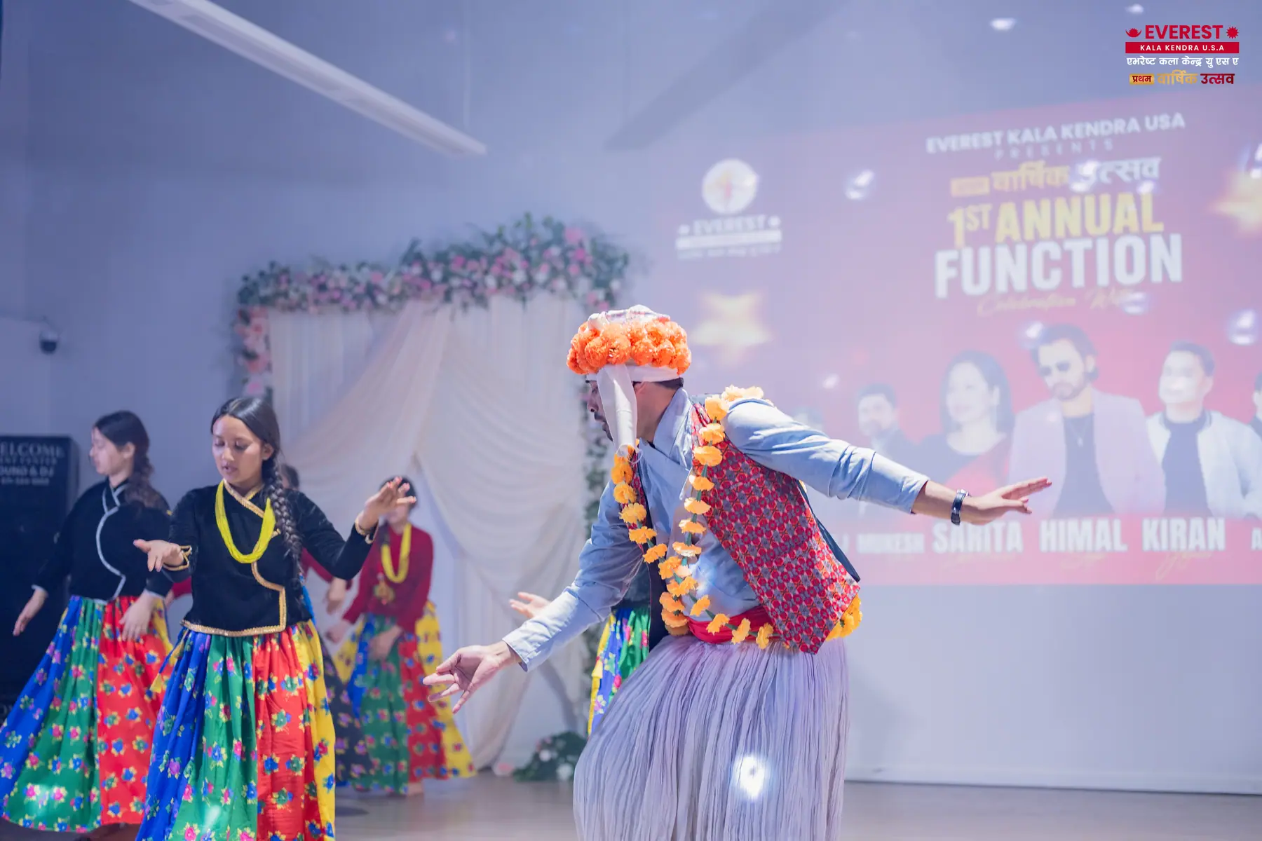 Two EKK dancers in elaborate traditional Nepali costumes performing with arms spread wide
