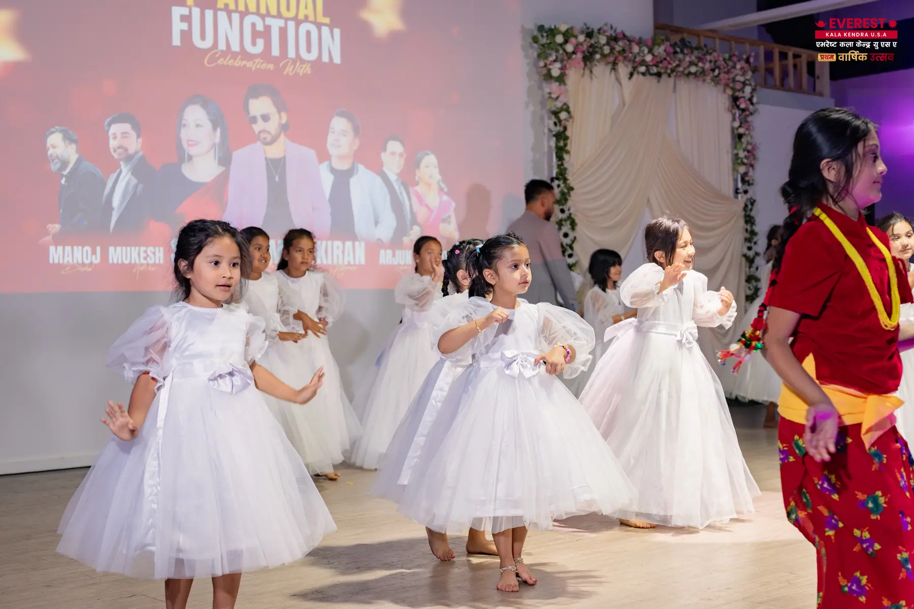 A group of young EKK students in white dresses holding a dance formation on stage