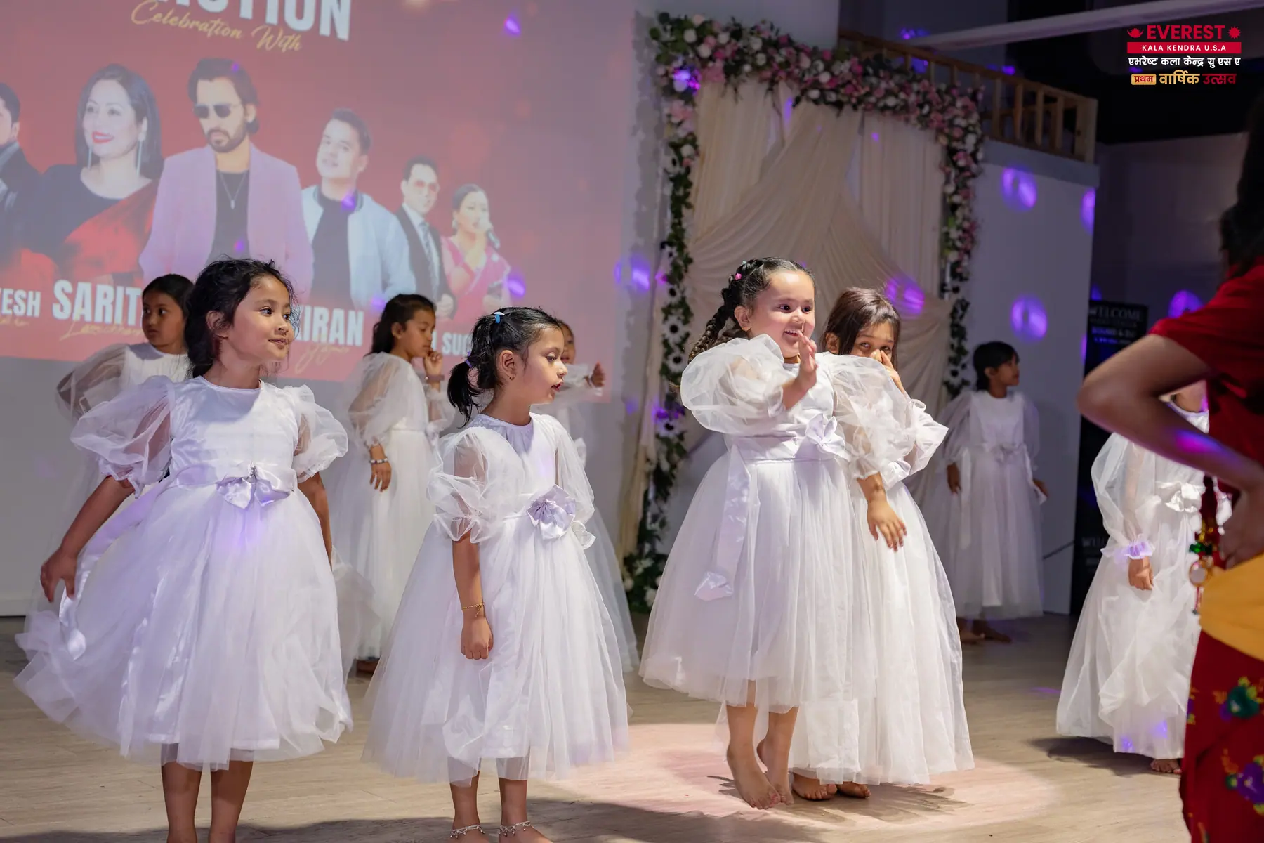 Several young EKK students in white dresses dancing together on stage
